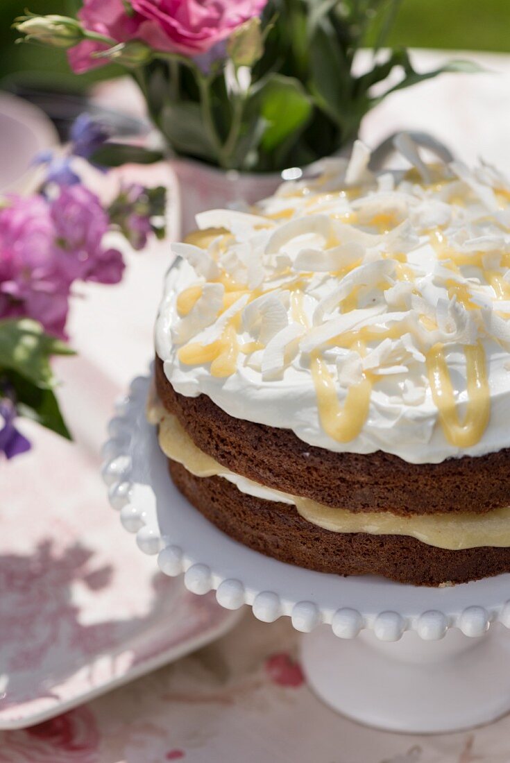 Summery lemon curd drizzle cake with coconut on a cake stand