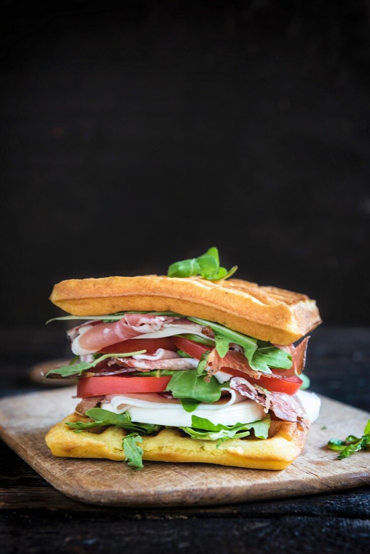 Ein Waffel-Sandwich mit Schinken, Tomate, Mozzarella und Rucola