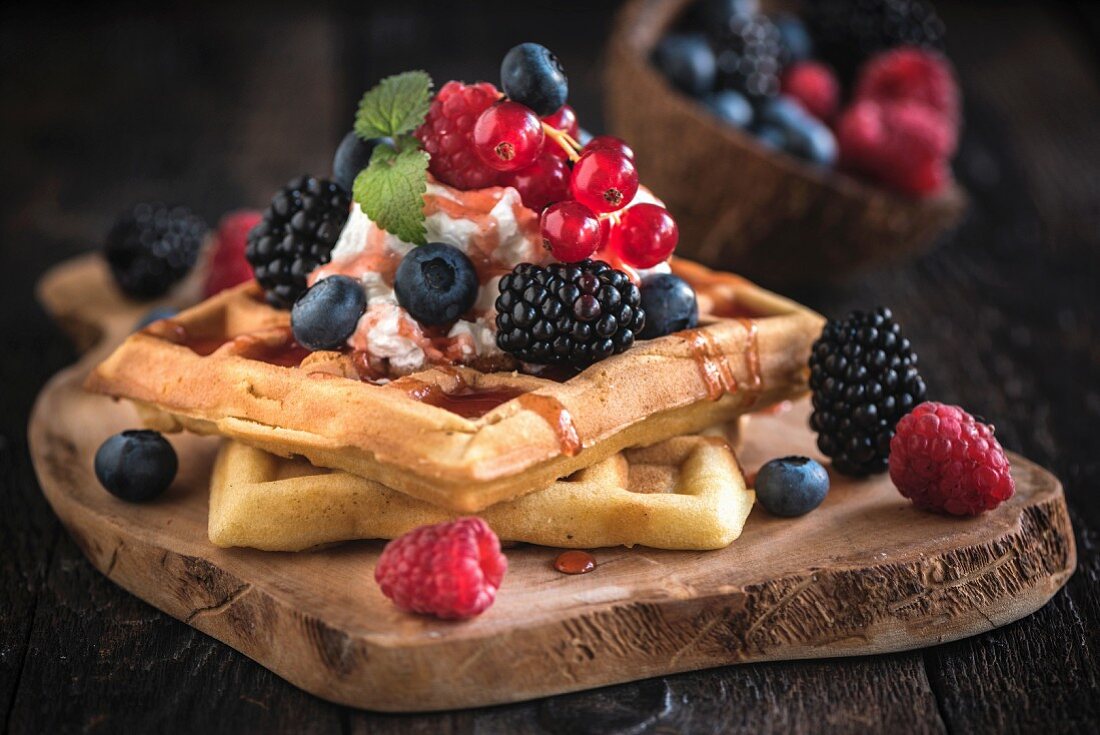 Belgian waffles with ice cream and berries on a wooden board