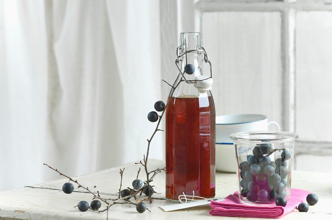 Schlehdornsirup in einer Flasche, Schlehdornfrüchte im Vorratsglas, Schlehenzweig und Schildchen
