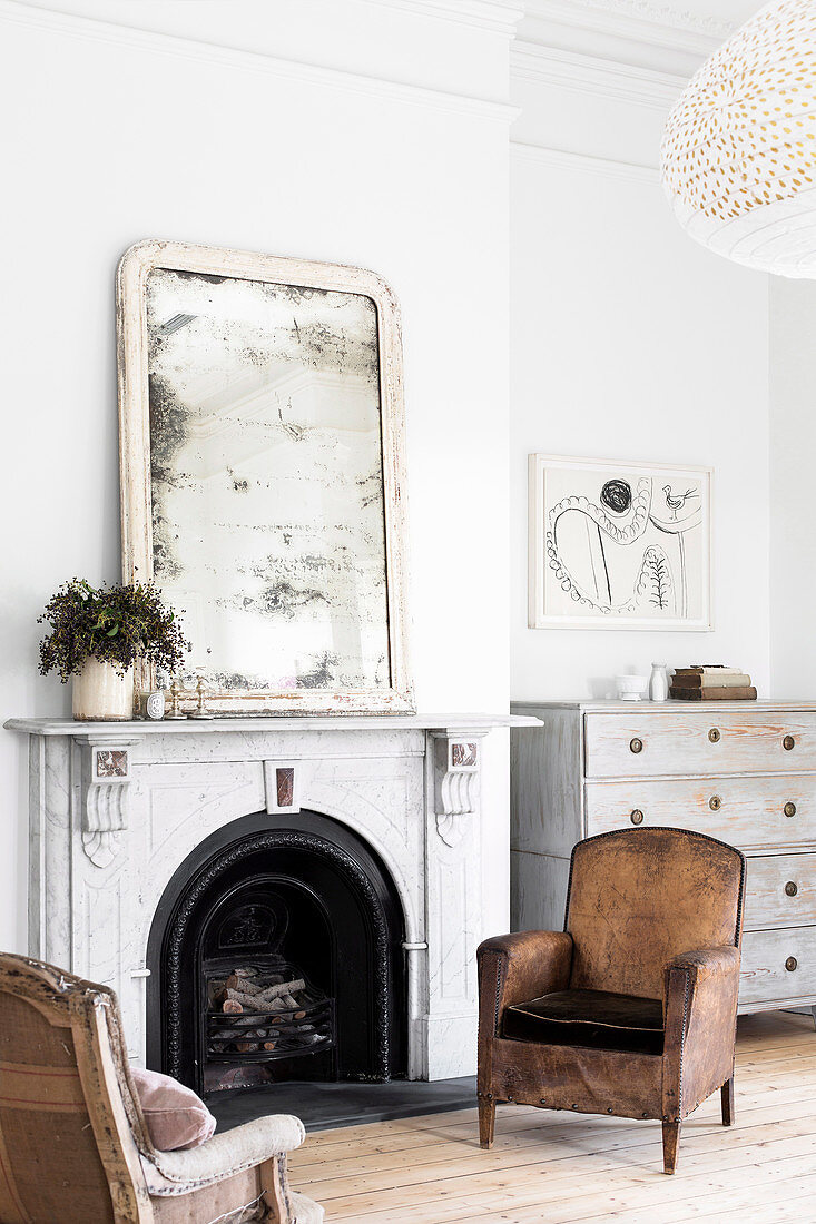 Two old armchairs in front of an open fireplace with a blind mirror on the console