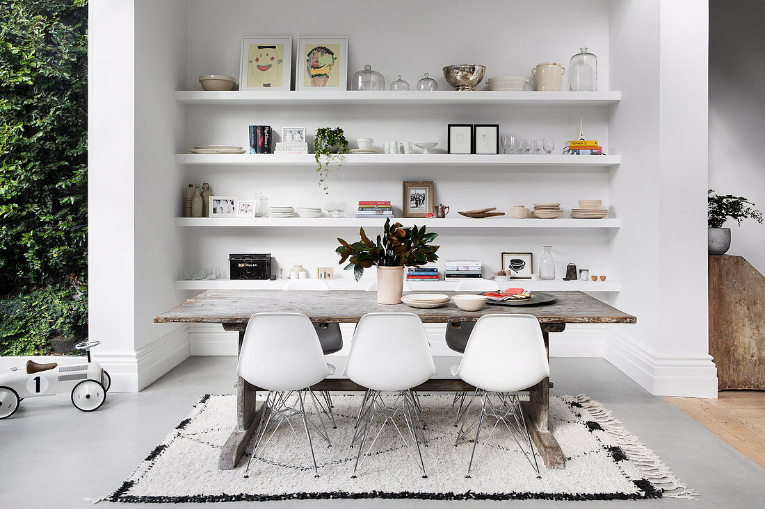 Designer chairs and a rustic wooden table in front of a niche with shelves