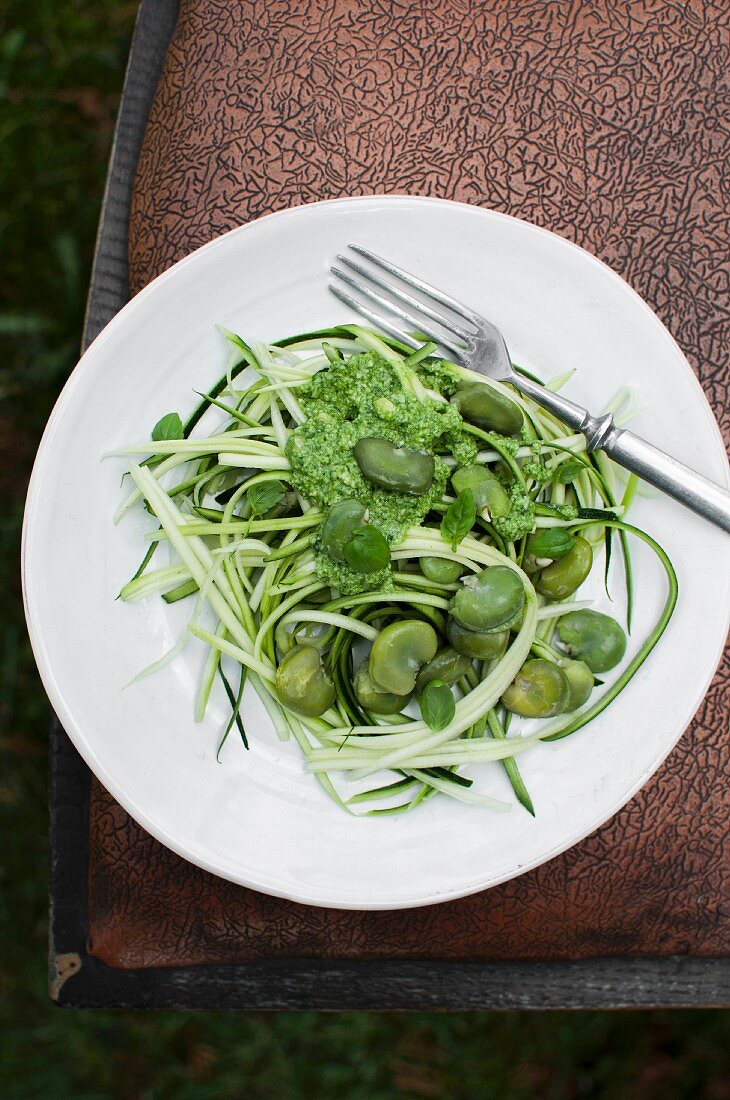 Raw zoodles (zucchini noodles) served with pesto and broad beans