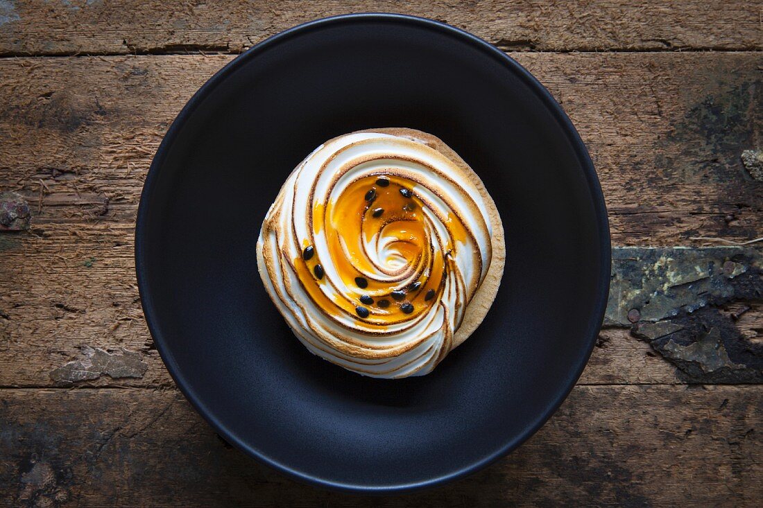 A passion fruit ad lemon meringue tart on a black bowl with a wooden background