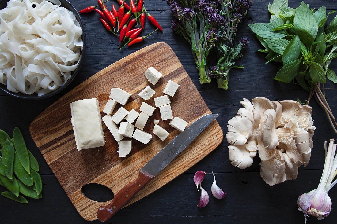 Zutaten für Pfannengericht mit Tofu, Brokkoli, Reisnudeln, Chilis, Thaibasilikum, Austernpilzen, Knoblauch und Zuckerschoten