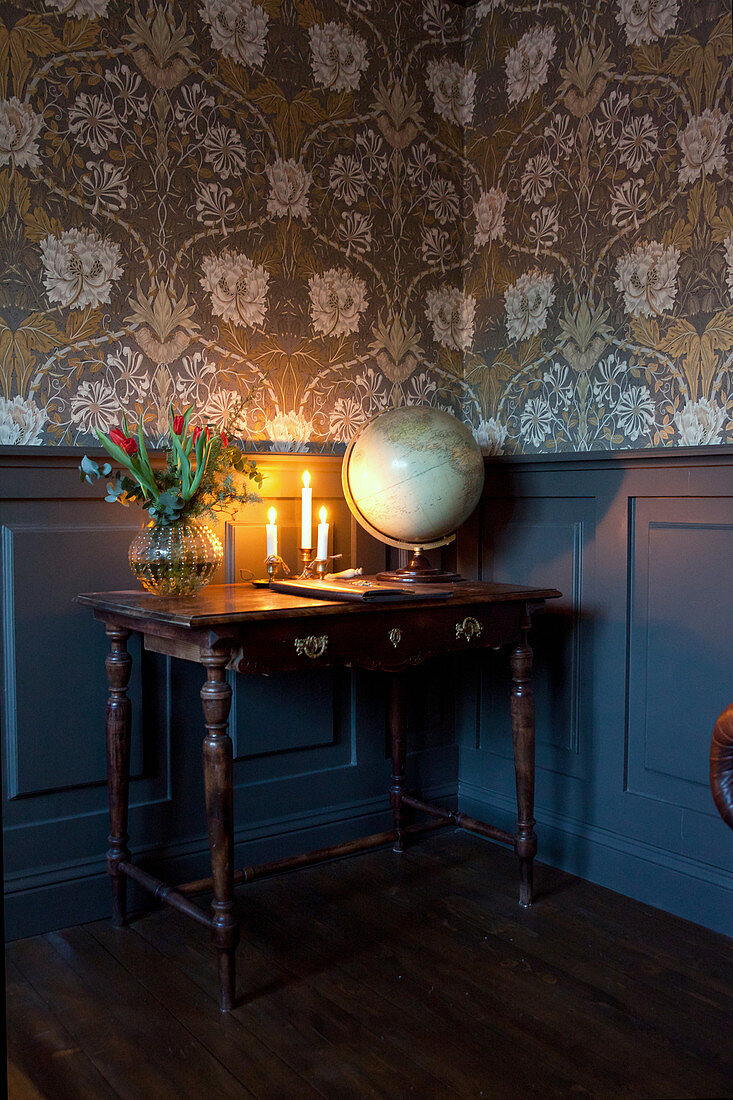 Wooden table against panelled wainscoting and below vintage-style wallpaper