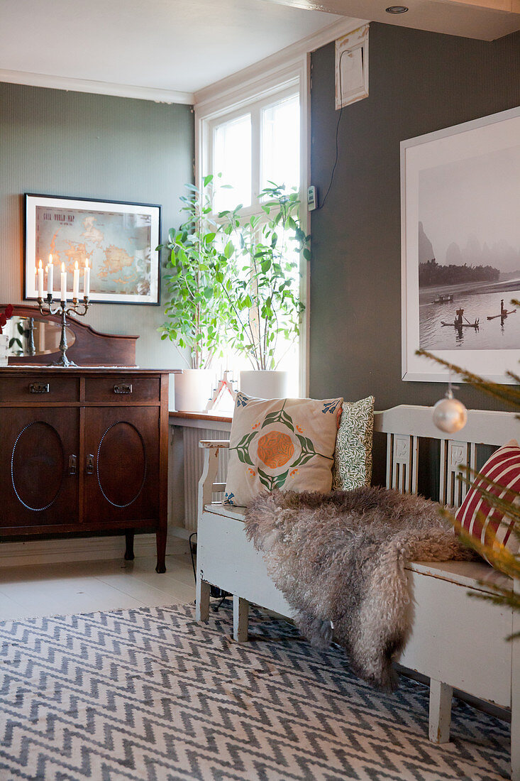 Cushions and fur blanket on traditional wooden bench on rug with zigzag pattern against grey wall