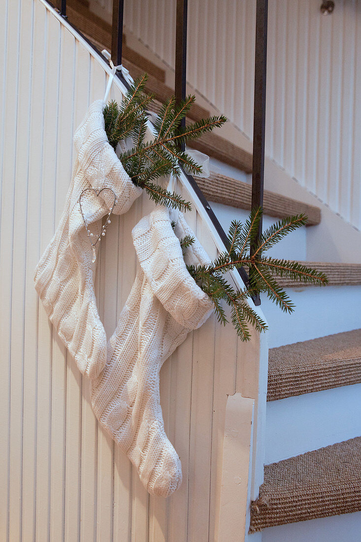 Zwei weiße gestrickte Weihnachtsstrümpfe mit Tannengrün an der Treppe
