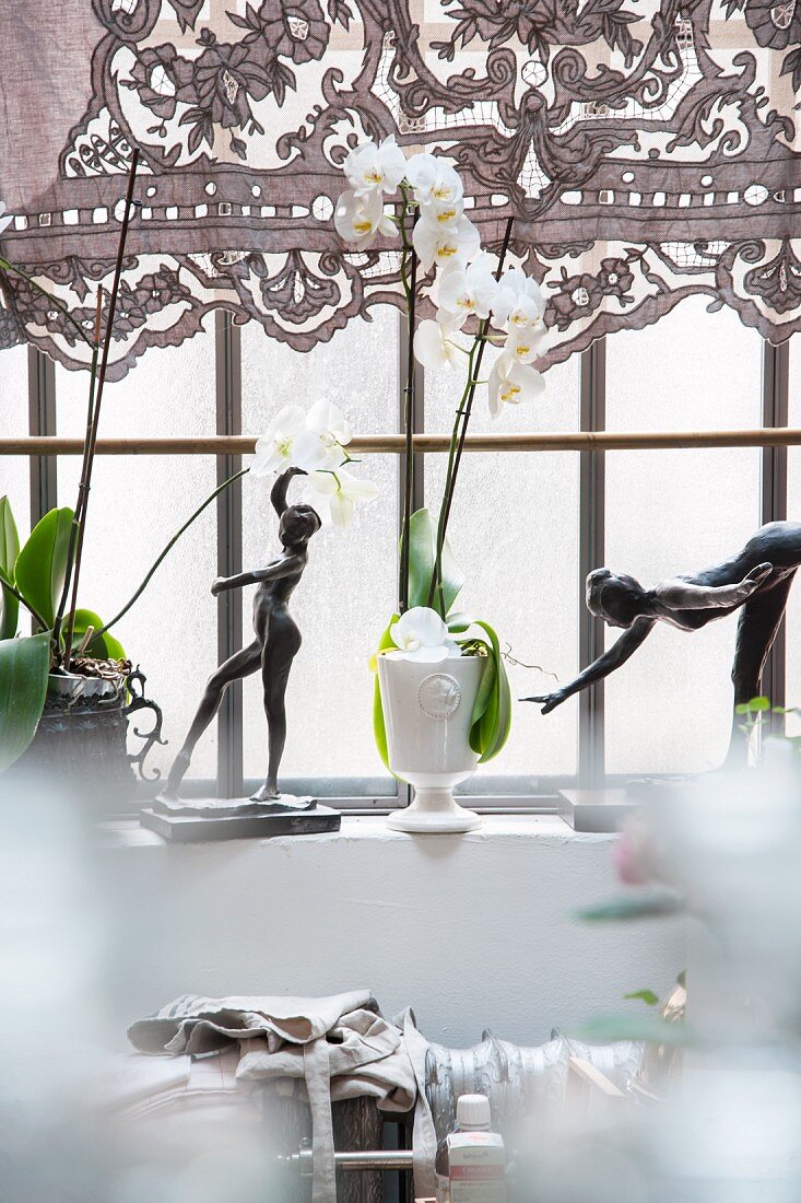 Two figurines of women and white orchid on windowsill