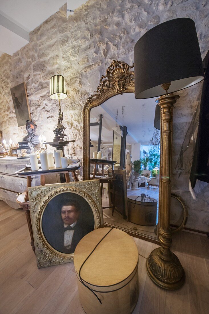 Antique portrait of man in front of gilt-framed mirror leant against stone wall