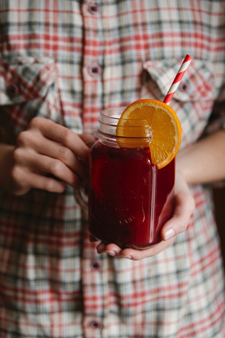 Frau hält ein Glas Früchtetee mit Strohhalm