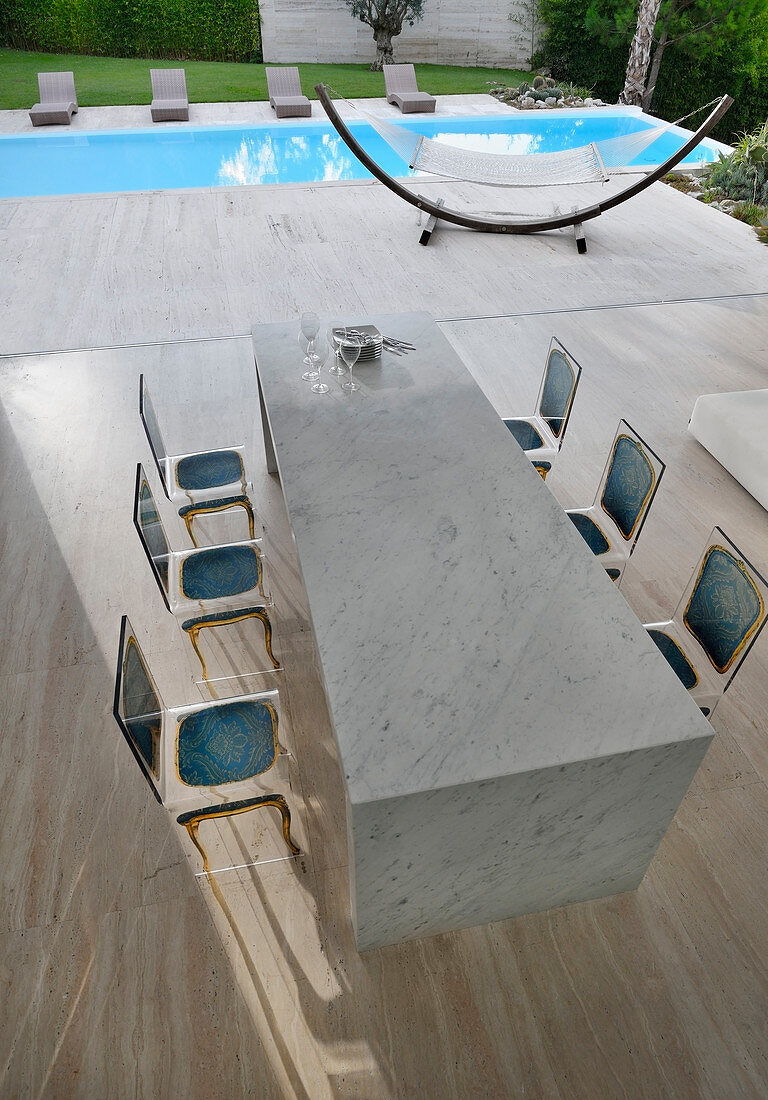 Marble table and acrylic Baroque-effect chairs in front of pool