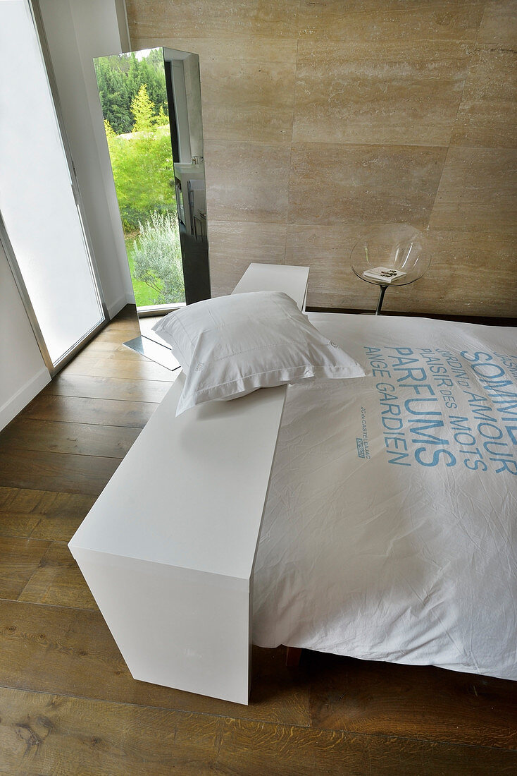 Table over bed in bedroom with wooden floor and stone wall