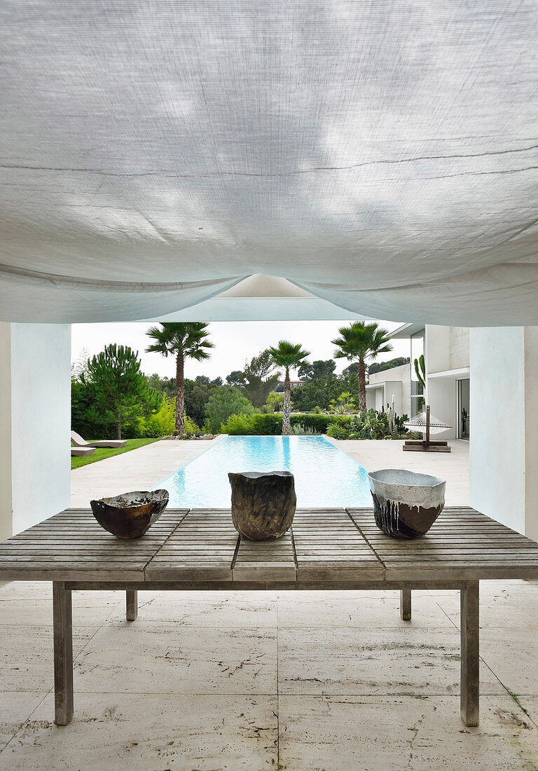 Ceramic bowls on wooden table under awning next to pool