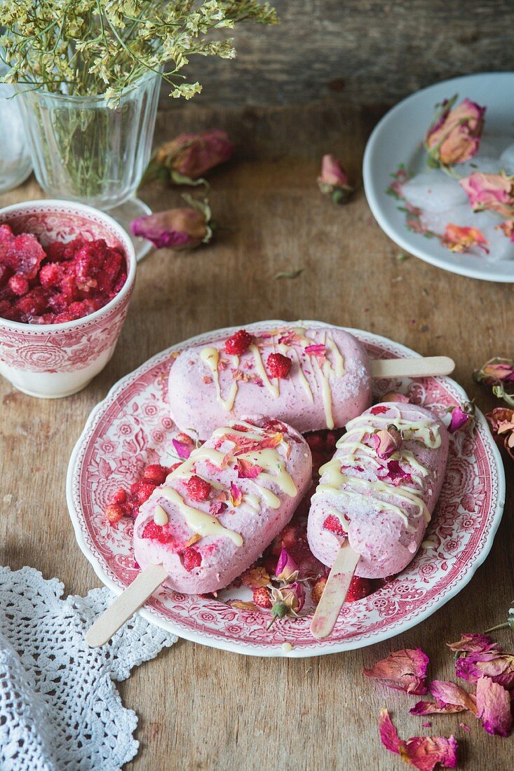 Erdbeereis am Stiel mit Walderdbeeren und Rosenblüten