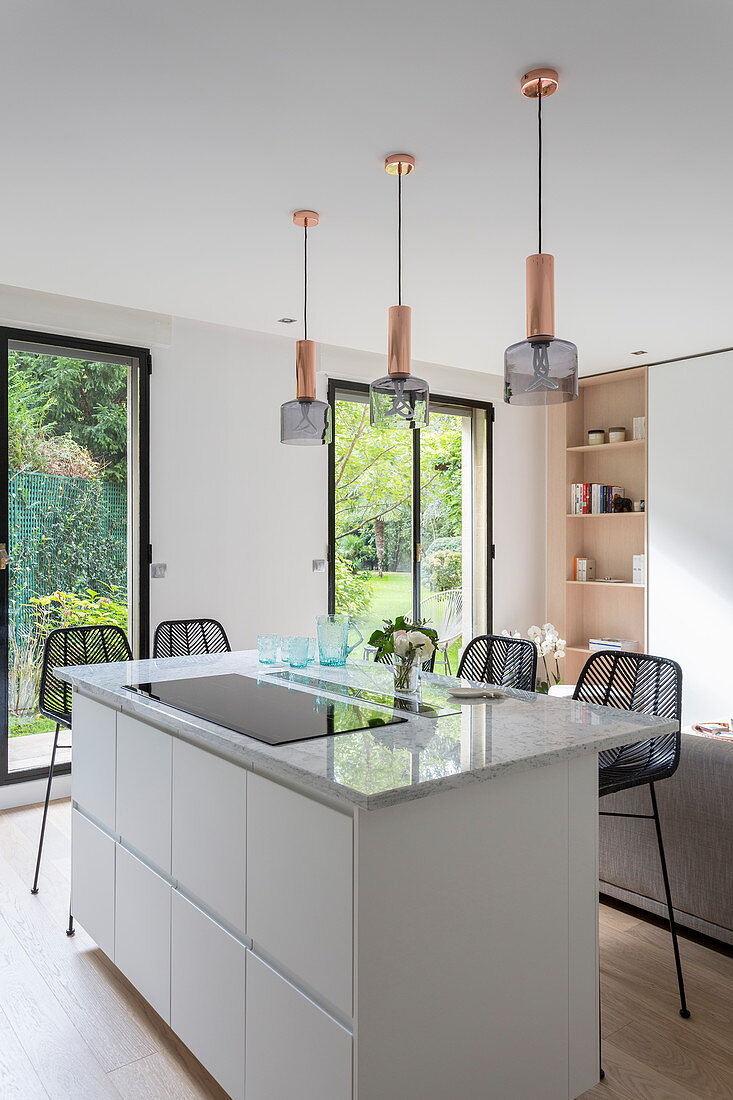 Lamps above island counter in front of floor-to-ceiling windows with garden view