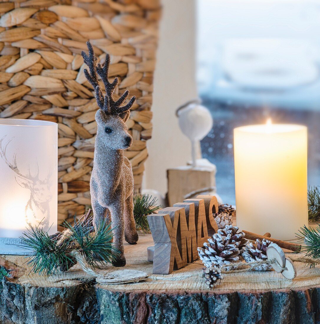 Rustic Christmas arrangement of reindeer figurine, candle, lantern and pine cones on slice of tree trunk