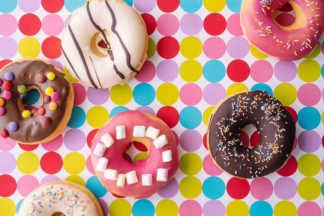 Bunt verzierte Donuts auf gepunkteter Tischdecke (Aufsicht)