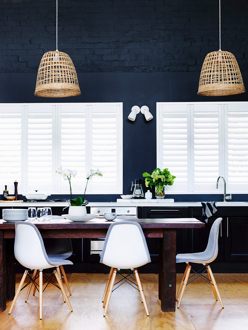 Dining table with replicas of classic chairs for windows and dark blue wall in open kitchen