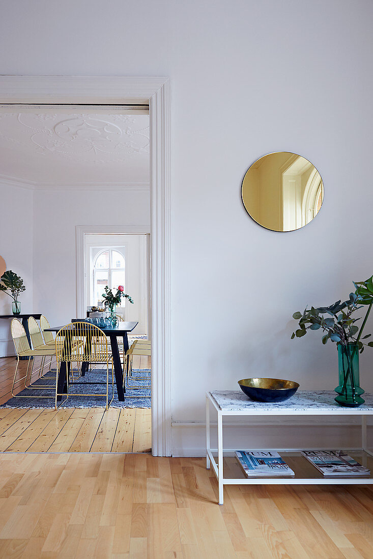 Side table below round mirror on wall and view into dining room