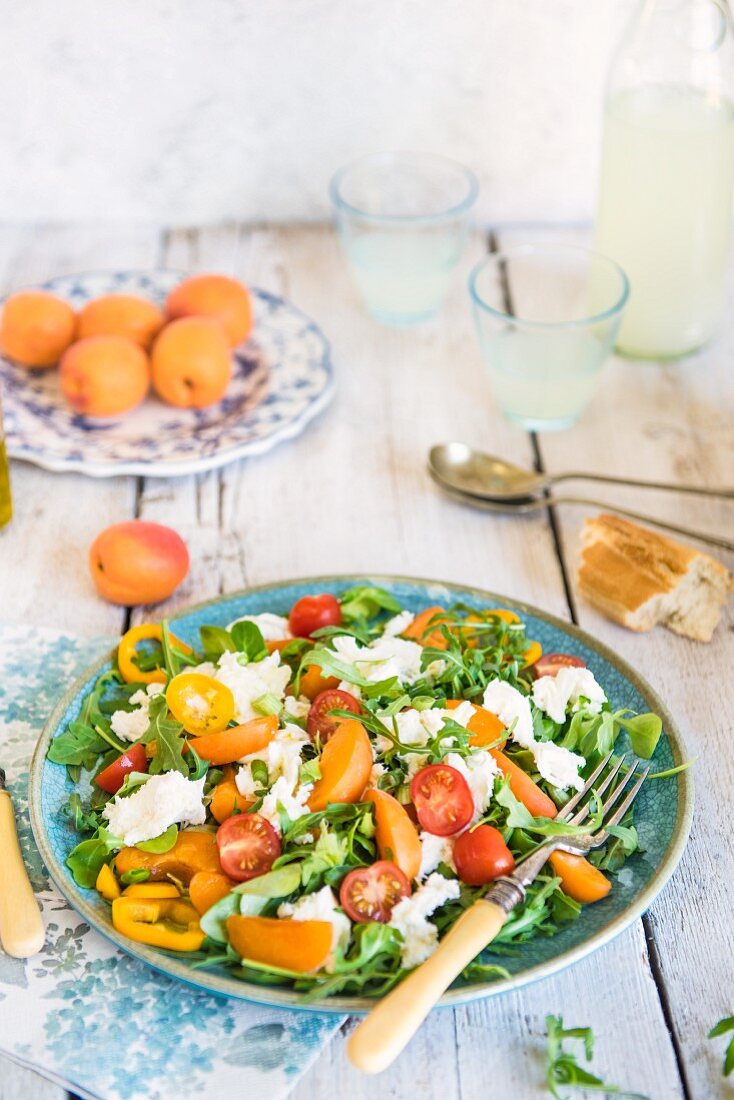 Salad with fresh apricots and mozzarella cheese, rocker, peppers and cherry tomatoes