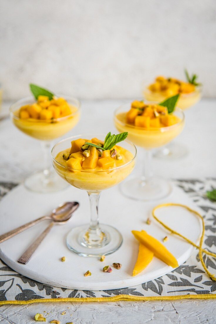 Mango mousse in stem glasses with mango chunks, pistachio nuts and fresh mint