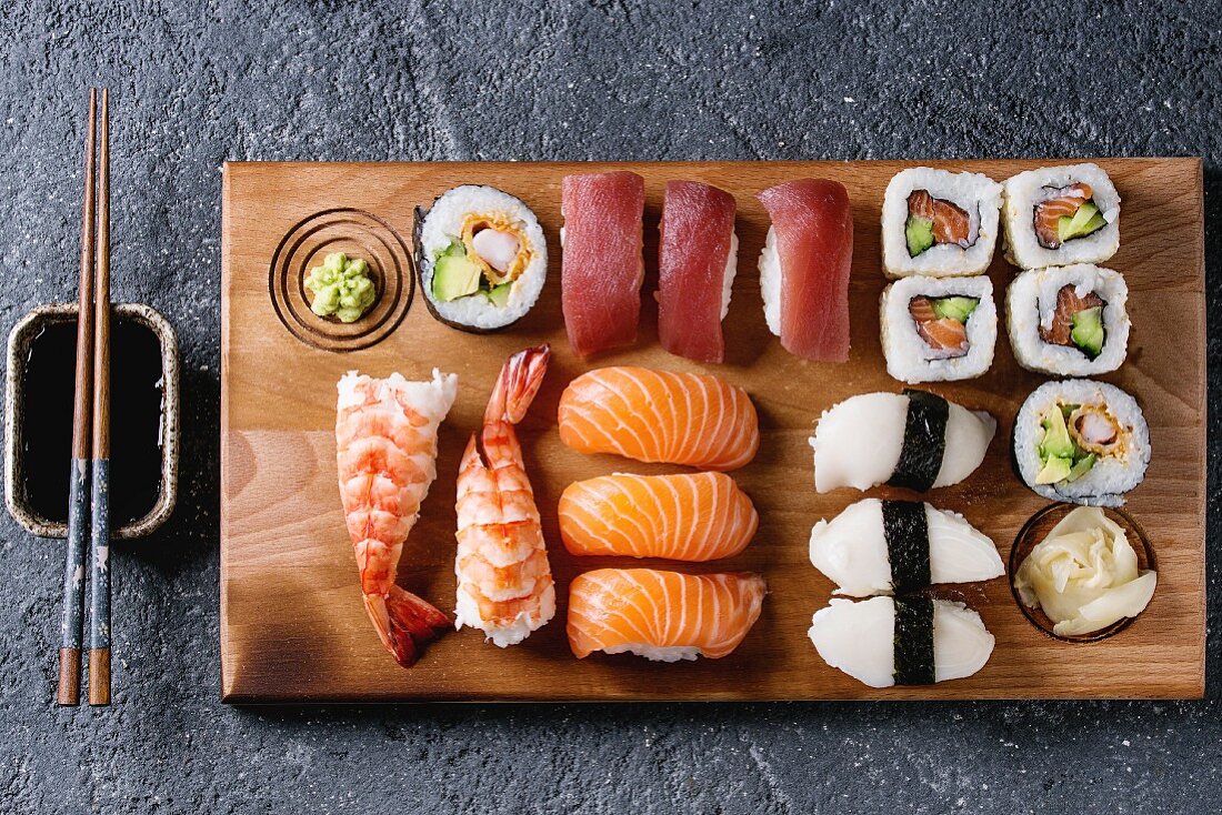 Nigiri-Sushi und Maki-Sushi auf Holzbrett daneben Sojasauce und Essstäbchen