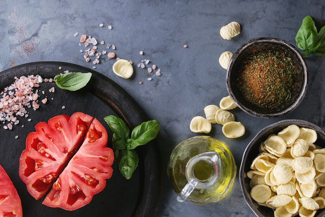 Homemade raw uncooked pasta with whole and sliced organic tomatoes Coeur De Boeuf, salt, seasoning, olive oil and basil