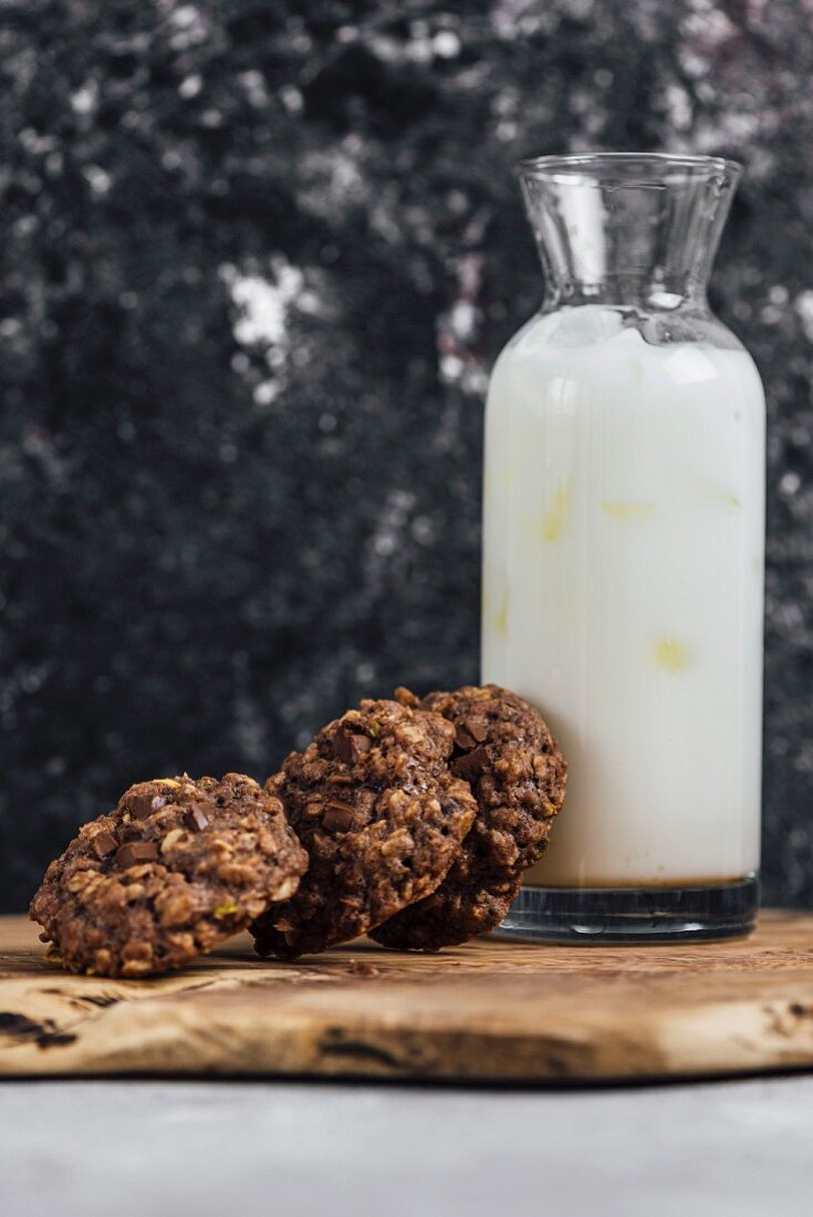 Chocolate zucchini oatmeal cookies leaned against a bottle of iced milk standing on a wooden board