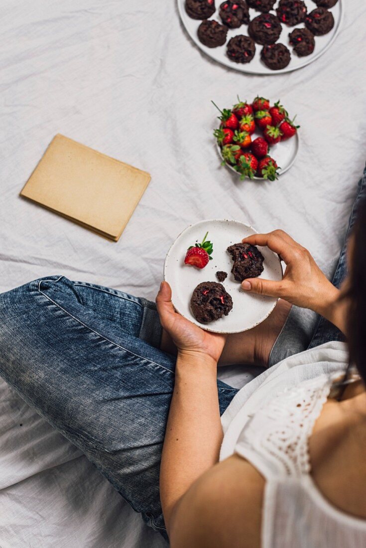 A woman with jeans sitting and eating cookies and fresh strawberries