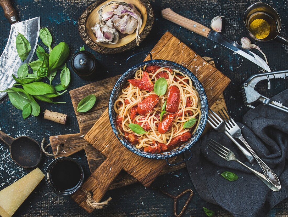 Italian style pasta dinner. Spaghetti with tomato and basil in plate on wooden board and ingredients for cooking pasta