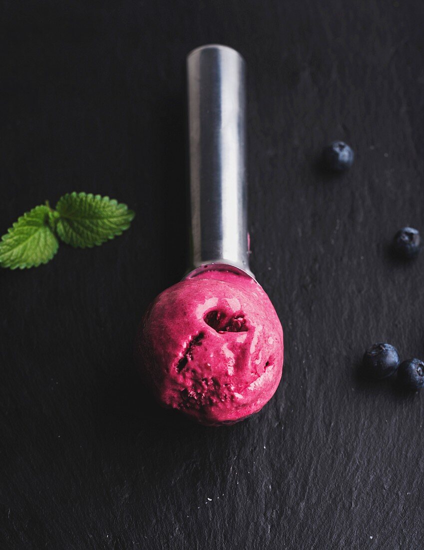 A scoop of blueberry ice cream on a black slate background