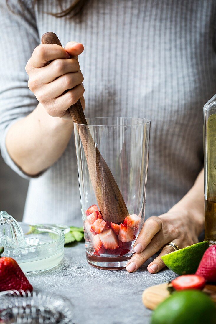Frau zerdrückt Erdbeeren für Erdbeer-Margaritas mit Holzstössel im Glas