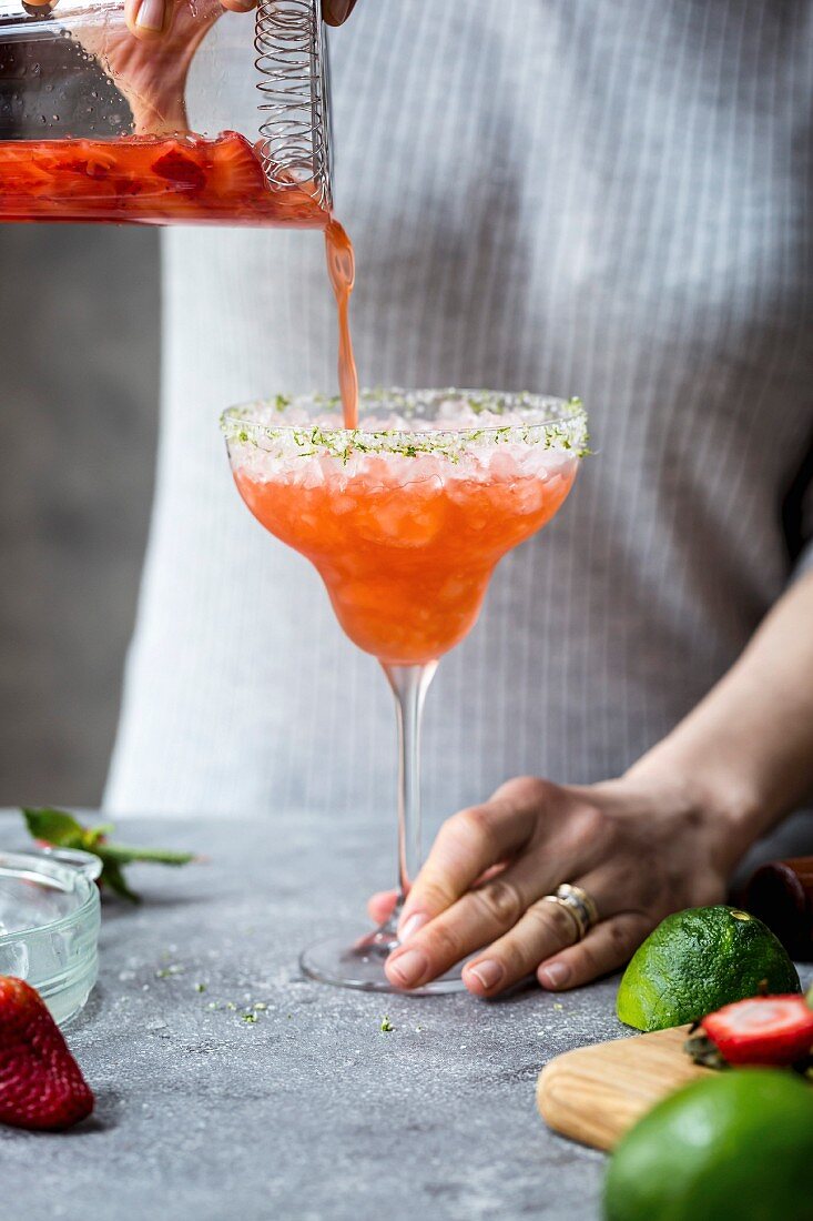 Frau giesst Erdbeer-Margarita in Margarita-Glas mit Crushed Ice