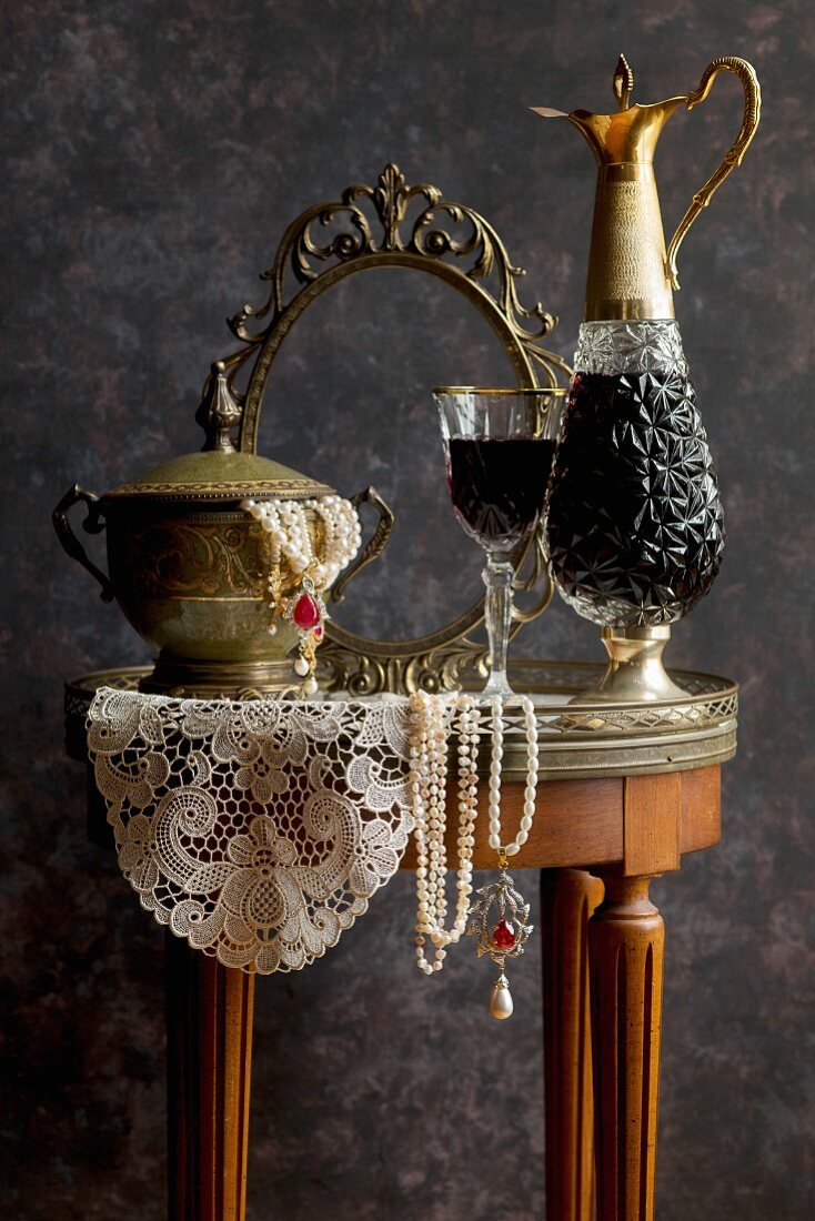 Stillleben mit Rotweinkaraffe und antiker Schmuckschatulle auf Tisch mit Spitzendeckchen
