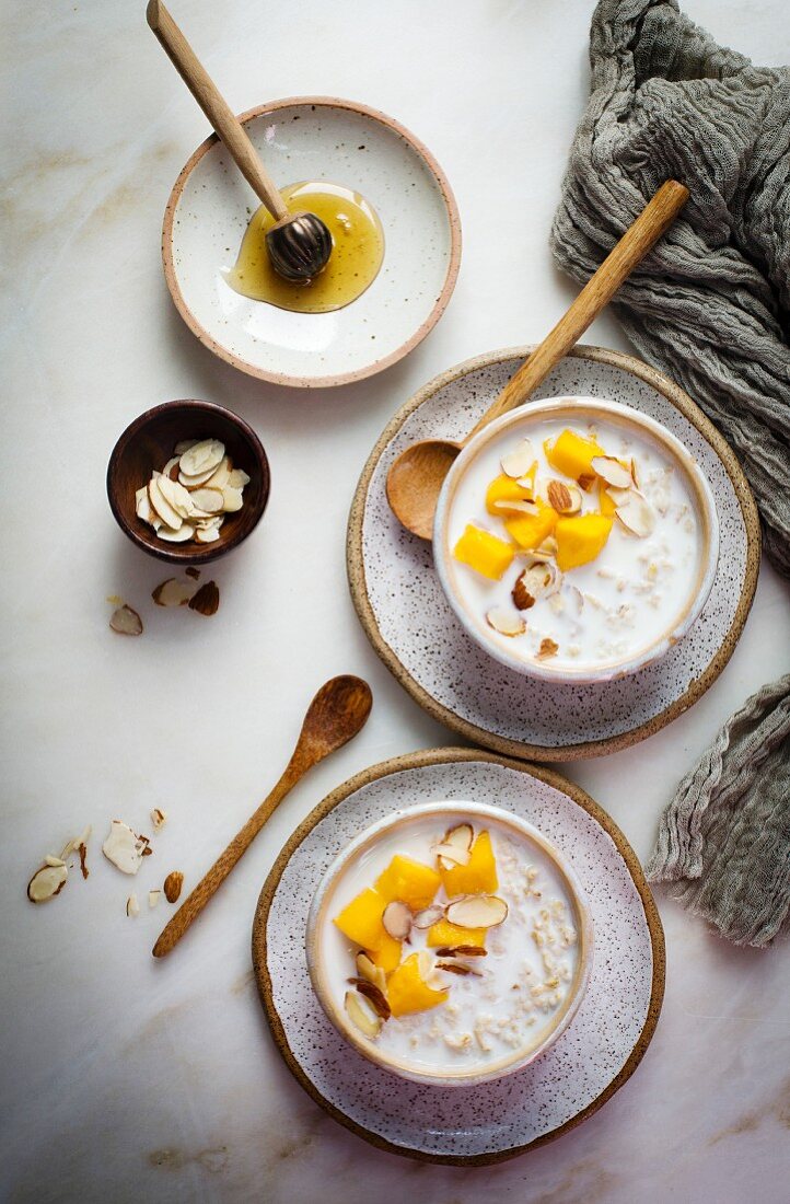 Oatmeal porridge with milk, mango, honey and almonds in small bowls