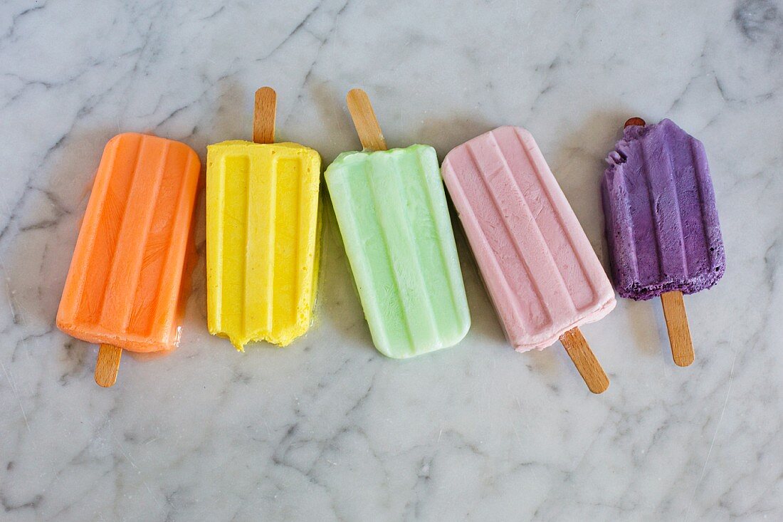 Five different coloured ice lollies on a marble background