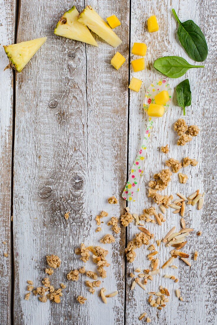 Pineapple, mango, spinach, crunchy muesli and almond slivers on a wooden background