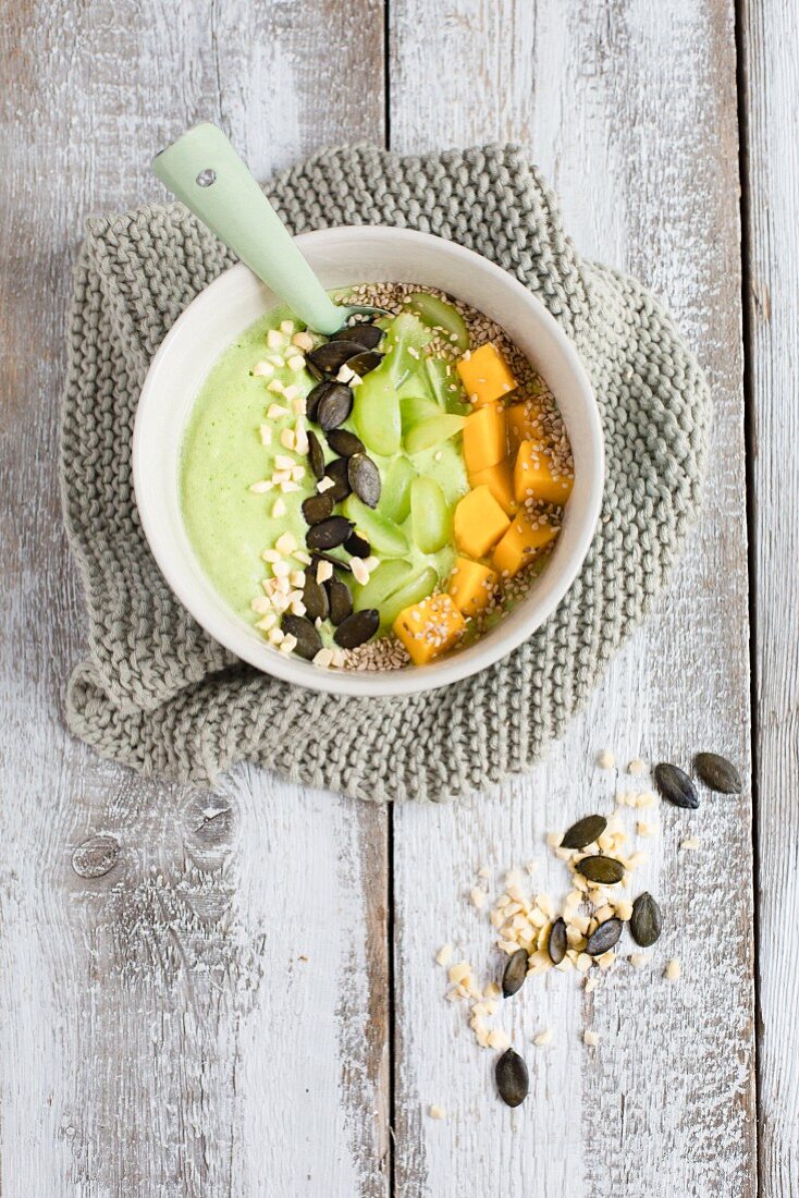 A green smoothie bowl with pumpkin seeds, grapes, mango and sesame seeds