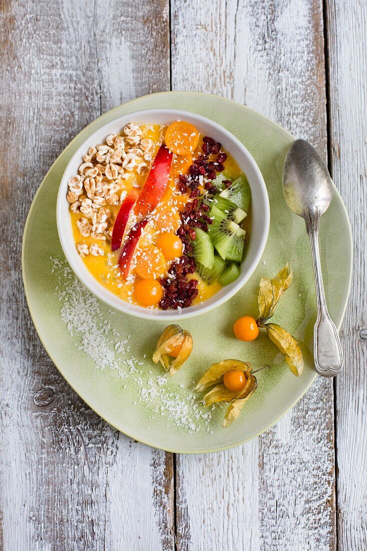 A yellow smoothie bowl with fruits, barberries and buckwheat pops