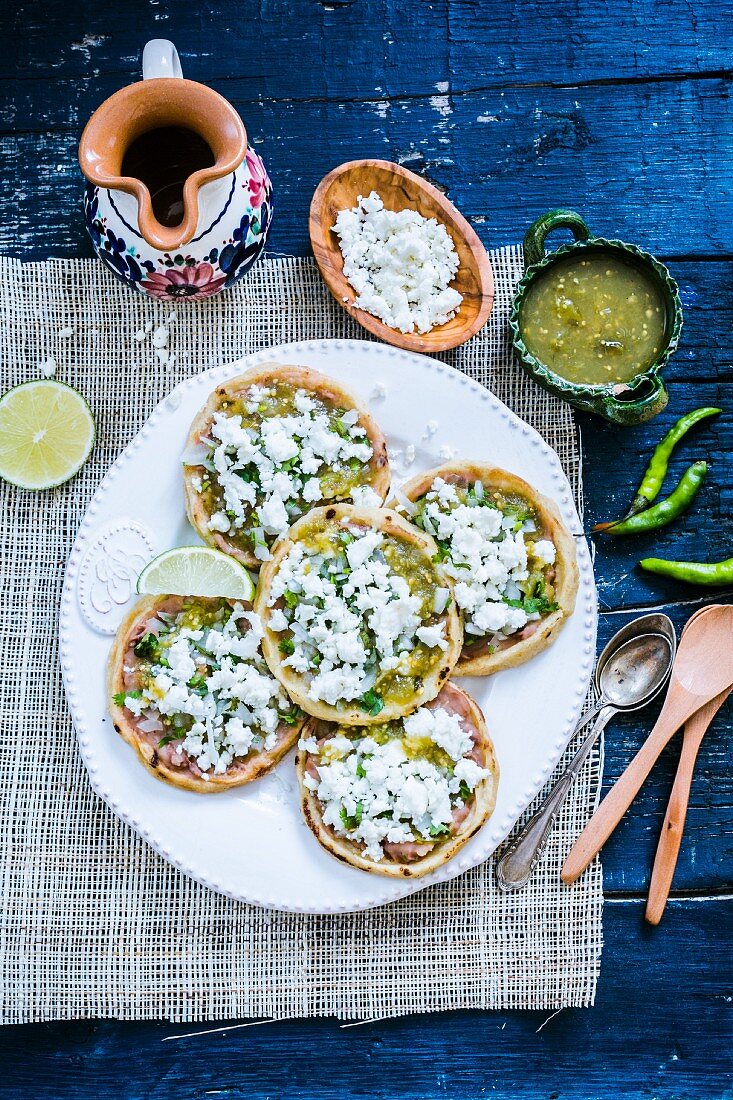 Mexikanische Maistörtchen mit Bohnen, Queso-Fresco (Frischkäse), gehackte Zwiebeln und grüner Chilisauce