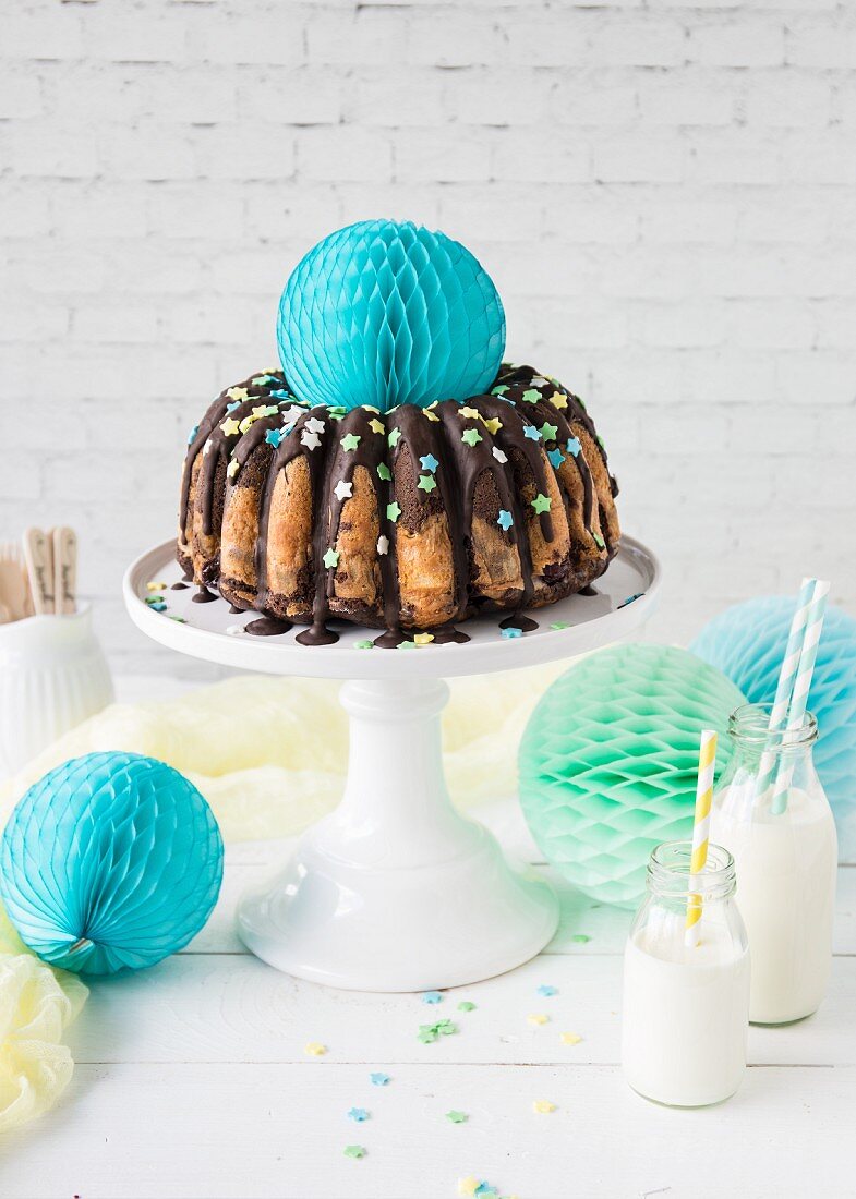 A gugelhupf with a chocolate glaze and colourful sugar stars, party decorations and milk bottles