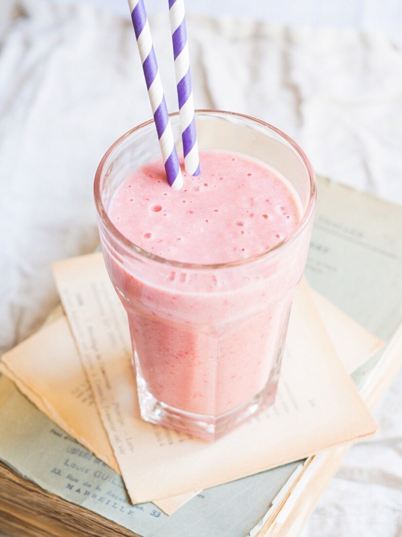 A strawberry smoothie in a glass with two drinking straws