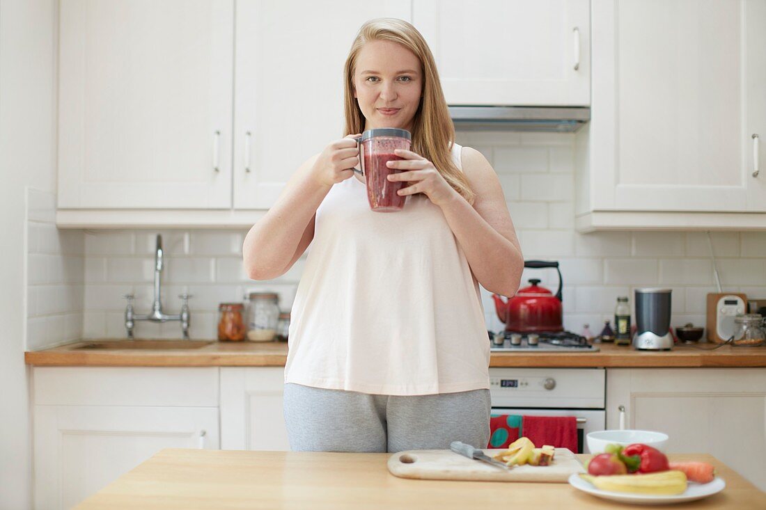 Young woman drinking smoothie in kitchen