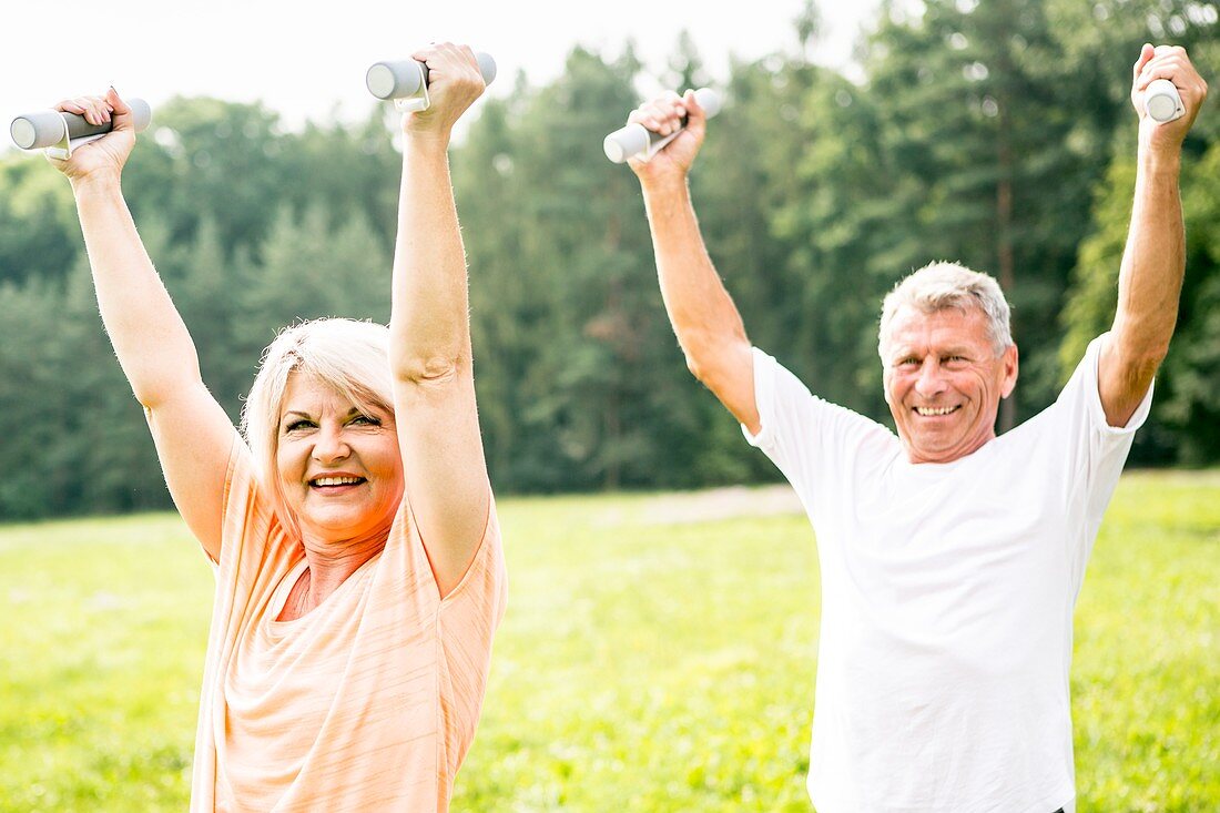 Mature couple exercising with hand weights in field
