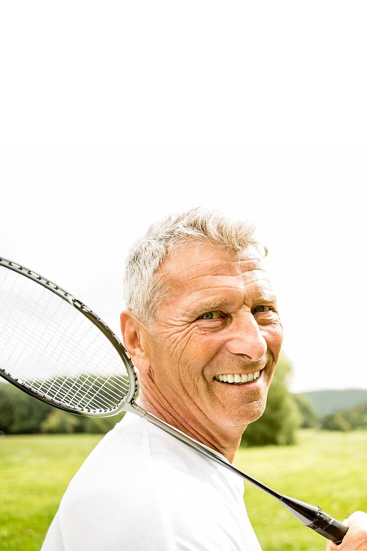 Man holding badminton rackets, smiling
