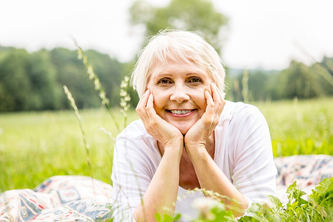 Senior woman lying on grass with hands on chin