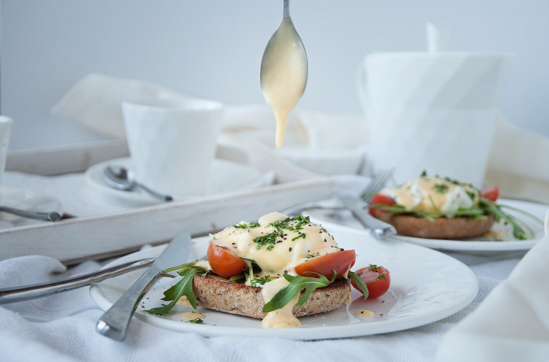 Eggs benedict with hollandaise sauce, rocket, and tomatoes on toast