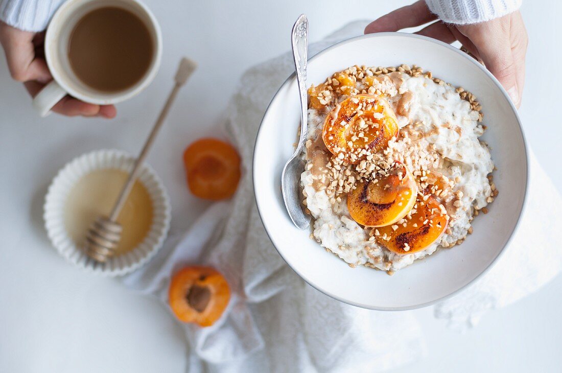 Porridge mit Aprikosen, Mandelbutter, Haselnüssen, Honig, Haferflocken, Cashewdrink, Kaffee