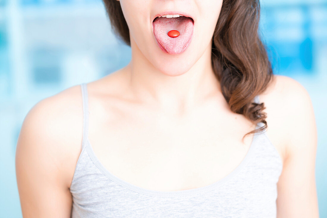 Woman with red pill on tongue